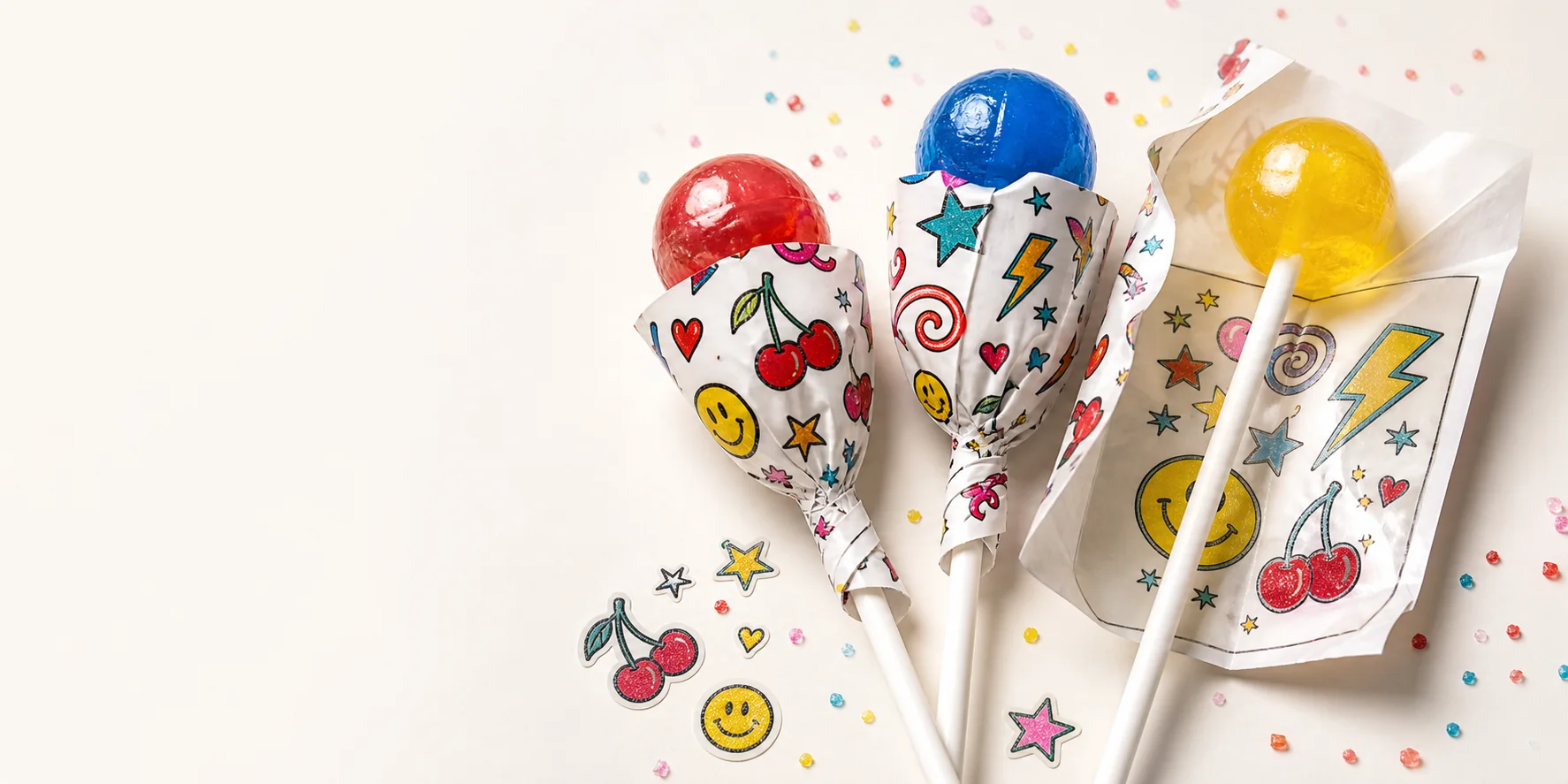 Three glossy lollipops wrapped in temporary tattoo sheets with cherries, stars, hearts, and lightning motifs